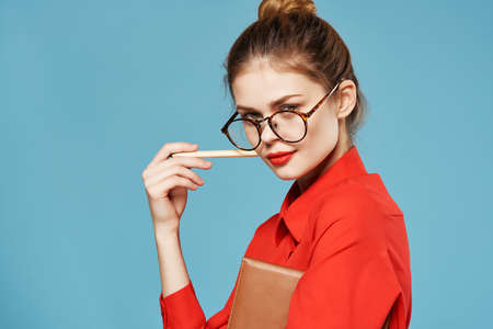 Business woman wearing glasses red shirt notepad with pencil blue backgroundの写真素材