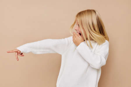 Beautiful little girl in a sweater, grimaces on a beige backgroundの写真素材