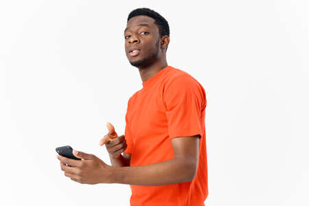 African American with a mobile phone and in an orange t-shirt on a light background