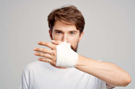 male patient in a white T-shirt with a bandaged hand posing isolated background