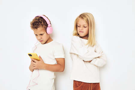 Two preschool children boy and girl headphones with phone entertainment isolated backgroundの写真素材
