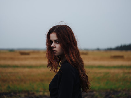 red-haired woman in black dress in a field landscape posing