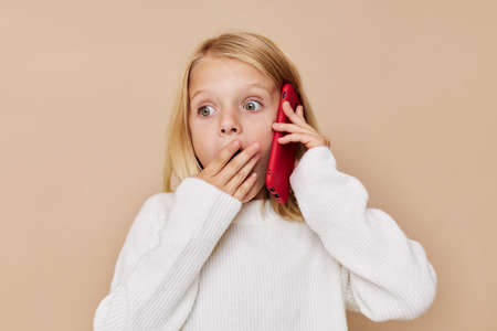 Little cute girl red phone in hand on a beige backgroundの写真素材