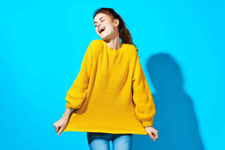 woman in yellow sweater holding hair blue background fashionの写真素材