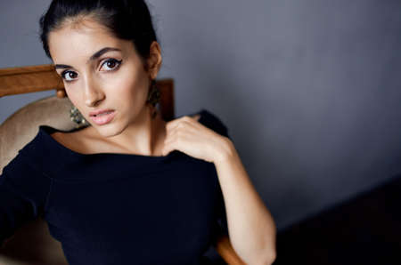 beautiful woman earrings jewelry posing near the chair black dress isolated backgroundの写真素材