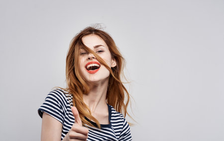 cheerful woman in a striped t-shirt gesture with his hands light backgroundの写真素材