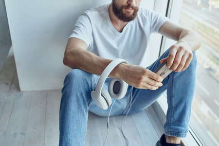 man in white t-shirt sitting near the window in headphones listening to musicの写真素材