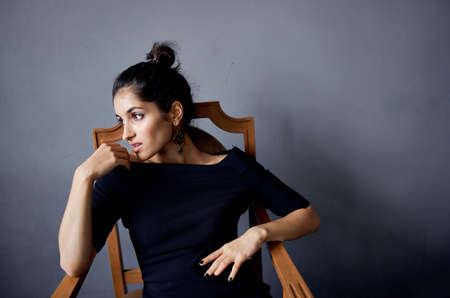 pretty woman earrings jewelry posing near the chair black dress isolated backgroundの写真素材