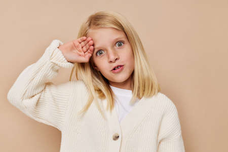 Little cute girl in a white sweater on a beige backgroundの写真素材