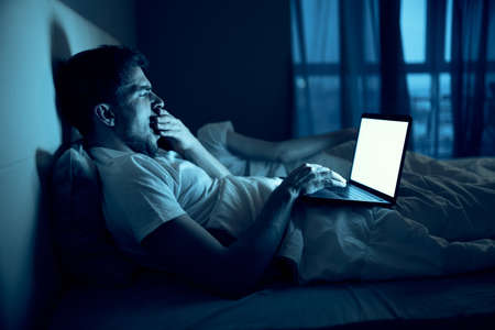 man at night in bed in front of laptop rest before bedtime