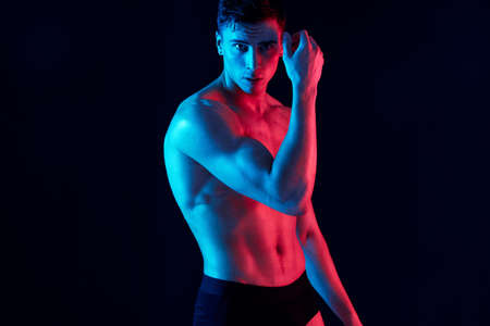 sexy guy with athletic physique posing on a black background and holds his hand near his faceの写真素材