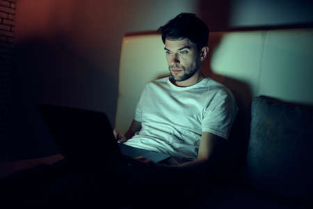 a man with a laptop lies in bed and looks at the monitorの写真素材