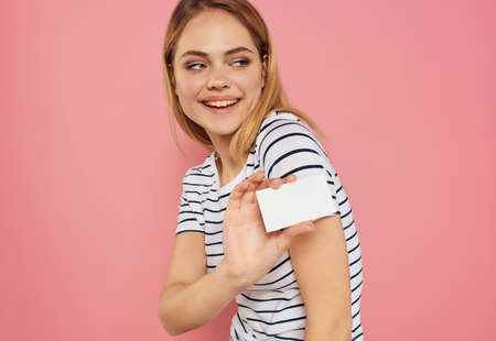 pretty woman in a striped T-shirt with a business card in hand pink backgroundの写真素材