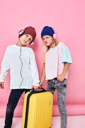 joyful boy and girl stylish clothes suitcase headphones isolated backgroundの写真素材
