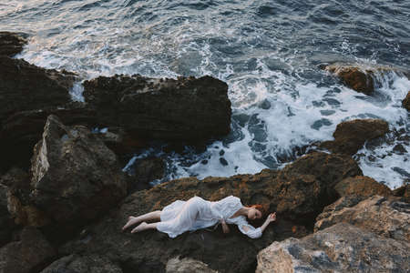 Beautiful bride lying on rocky coast with cracks on rocky surface view from aboveの写真素材
