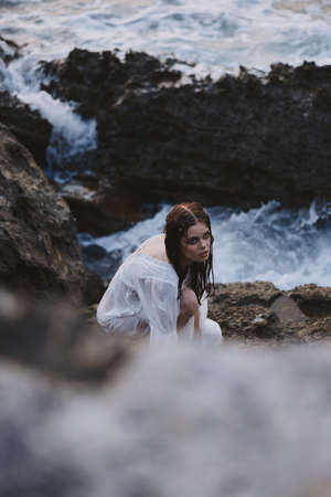 woman with wet hair in white dress on a rocky stone ocean natureの写真素材