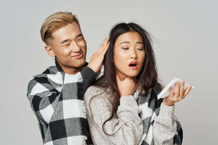 man caring for a woman with a cold on a gray background and a napkin in his handの写真素材