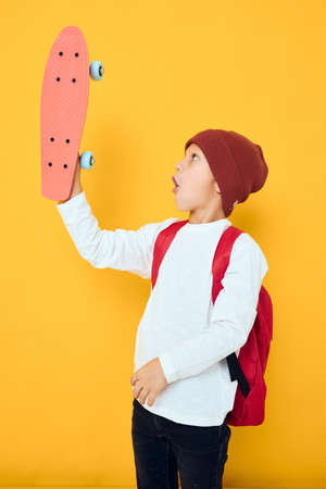 Cheerful little kid in a red hat skateboard in his hands yellow color background