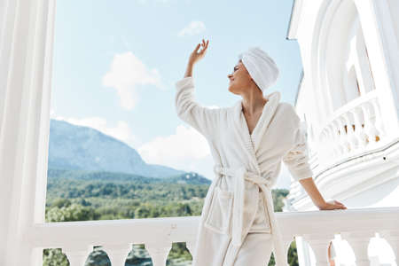 beautiful woman with a towel on my head in a white bathrobe staying on the balcony in a hotel Relaxation conceptの写真素材