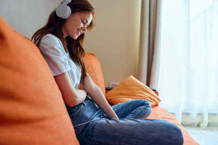 beautiful woman sitting on the couch at home listening to music on headphones Lifestyle