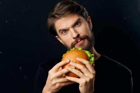 man with hamburger in his hands fast food gourmet restaurant dark backgroundの写真素材