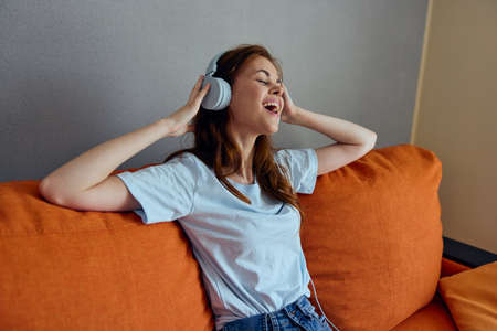 woman sitting on the couch at home listening to music on headphones technologies