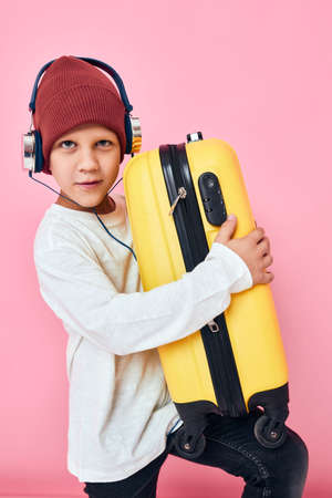 cute boy holding suitcase in hands headphones pink backgroundの写真素材