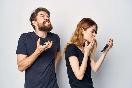 cheerful young couple in black t-shirts phone fun together friendship light backgroundの写真素材