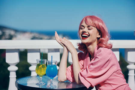 cheerful woman with pink hair sitting at the table outdoors cocktailの写真素材