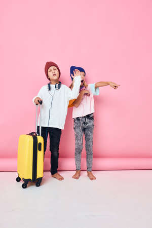 Portrait of a girl and a boy yellow suitcase with headphones pink color background