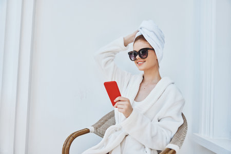 cheerful woman uses a red phone in a chair in a white robeの写真素材