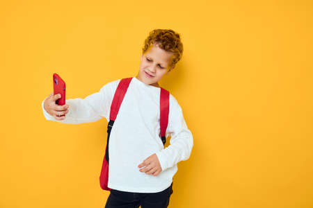 teenager boy talking on the phone with a school backpack yellow backgroundの写真素材