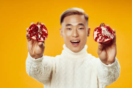 Cheerful man of Asian appearance in a white sweater with a pomegranate in his handsの写真素材