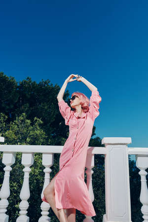 glamorous woman pink dress modern style stands near the railing sunny dayの写真素材