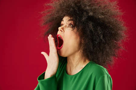 Pretty young female Afro hairstyle green dress emotions close-up red background unalteredの写真素材