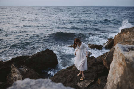 a woman in a wedding dress stands by the ocean on a cliffの写真素材