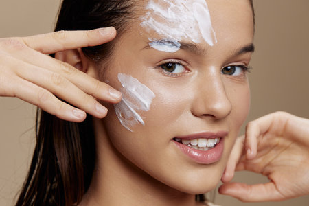 beautiful woman with moisturizer on the cheeks in the eye area beige backgroundの写真素材