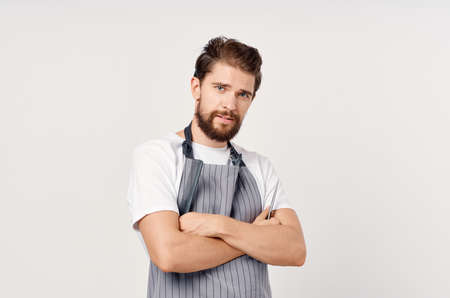 confident hairdresser in an apron with a comb and scissors in his hands gestures with his hands and...