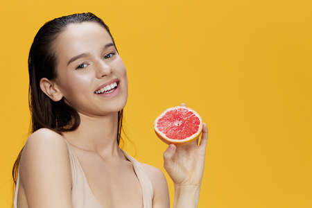 brunette eating grapefruit in hands smile vitamins diet yellow backgroundの写真素材
