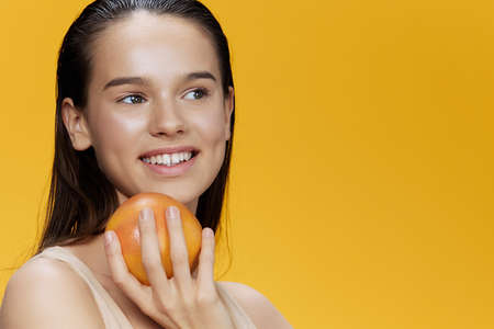 young woman with grapefruit near face clean skin care health yellow backgroundの写真素材