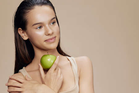 young woman green apple near face health beige background