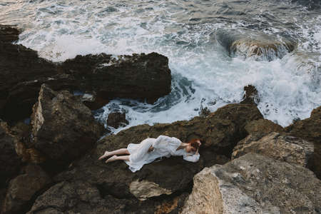 woman in a secluded spot on a wild rocky coast in a white dress vacation conceptの写真素材