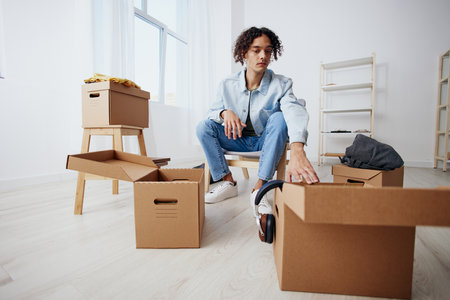 guy with curly hair sitting on a chair with boxes moving sorting things out