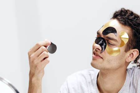 A young man black and gold patches on the face health cosmetology light background