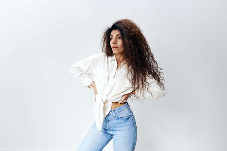 Sexy Curly Pretty Pensive Latin Female Lady in White Shirt tied in bow Holding Hands On Waist copy space, free place Looking Aside Isolated At White Studio Wall Background. Good Offer, Banner, Mockupの写真素材
