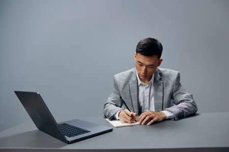 businessmen sitting at a desk in front of a laptop work writing in a notebook isolated background