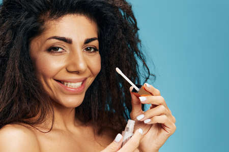 Close up portrait of cheerful happy tanned pretty curly Latin female hold lipstick smile at camera...
