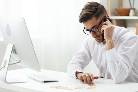 handsome businessman in a white shirt sits at a computer with a phone office