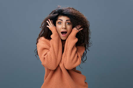 SENSATION CONCEPT. Excited tanned curly Latin female in warm sweater recline on hands say Wow open mouth posing isolated over gray blue background look at camera. Copy space Mockup Banner. Cool offerの写真素材
