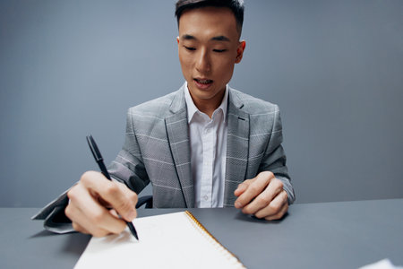 business man of Asian appearance in a gray suit writes on the tableの写真素材